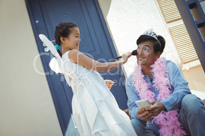 Cute daughter in fairy costume putting makeup on her fathers face