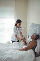 Female doctor giving sick senior woman a glass of water on bed