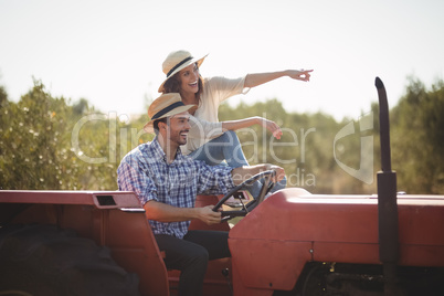 Cheerful woman gesturing away while sitting with boyfriend on tractor