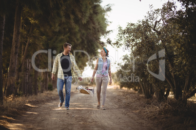 Cheerful couple carrying basket while walking on dirt road at olive farm