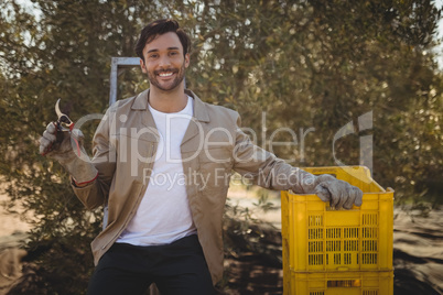 Smiling young man with pliers and crates at farm
