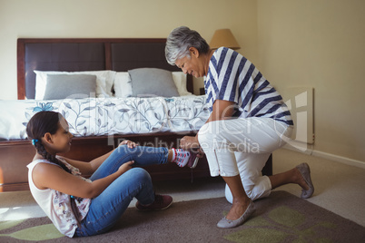 Grandmother helping granddaughter to wear shoes in bed room