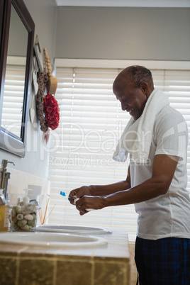Side view of smiling senior man holding toothpaste and brush in bathroom