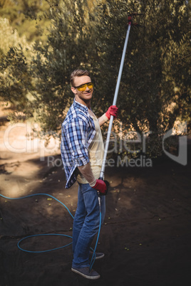 Portrait of smiling man using olive rake at farm