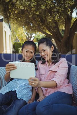 Mother and daughter relaxing on couch and using digital tablet