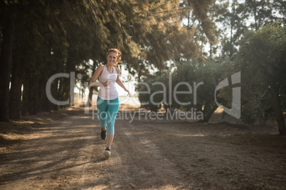 Smiling young woman jogging on dirt road during sunny day
