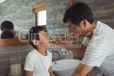 Father brushing his sons teeth in bathroom