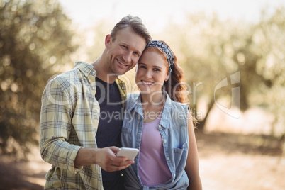 Smiling young couple with mobile phone at olive farm