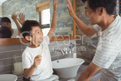 Father and son giving high five to each other in bathroom