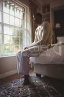 Full length of thoughtful man sitting on bed by window