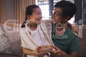 Daughter giving gift box to father in living room