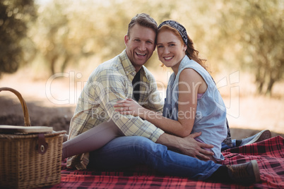 Cheerful couple sitting on mat at olive farm