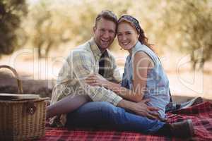 Cheerful couple sitting on mat at olive farm