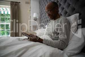 Smiling senior man reading book while relaxing on bed