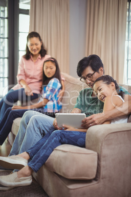 Smiling family using digital tablet together in living room