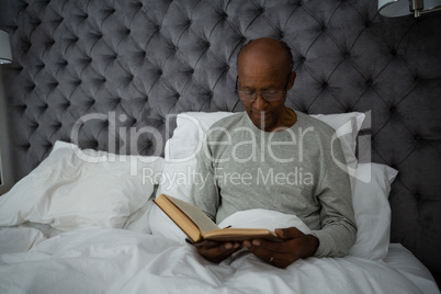 Senior man reading book while sitting on bed