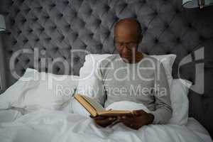 Senior man reading book while sitting on bed