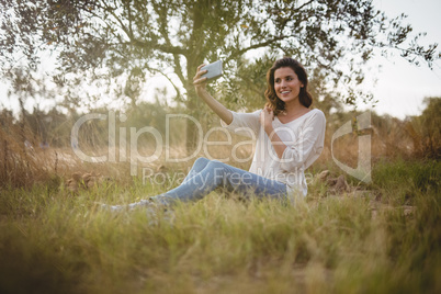 Beautiful woman taking selfie while sitting on grassy field