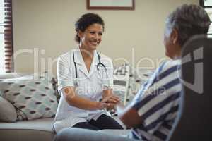 Female doctor comforting senior woman in living room