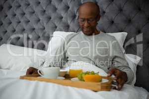Smiling senior man having breakfast in tray on bed