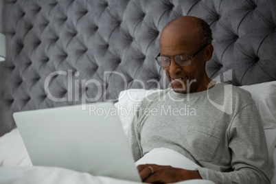 Senior man using laptop on bed at home