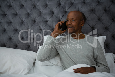 Happy senior man talking on mobile phone in bedroom