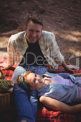 Portrait of smiling couple resting on field at farm