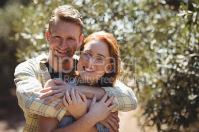 Happy couple embracing by trees at olive farm