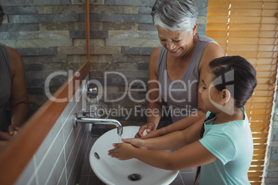 Grandmother and granddaughter washing hands in bathroom sink