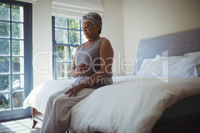 Upset senior woman touching belly at home