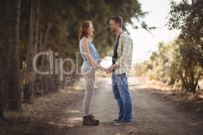 Young couple holding hands while standing on dirt road at olive farm