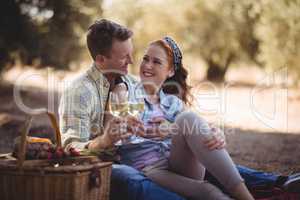 Young man and woman looking at each other while holding wineglasses at farm
