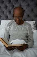 Smiling senior man reading book while sitting on bed