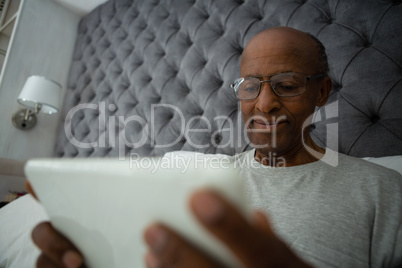 Senior man using digital tablet while relaxing on bed