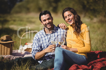 Portrait of happy couple holding wineglasses while sitting on picnic blanket