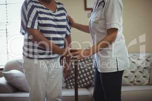 Female doctor helping senior woman to walk with walking stick