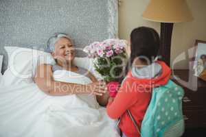 Granddaughter giving flowers to grandmother in bed room