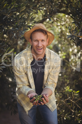Cheerful young man holding olives while standing by trees at farm