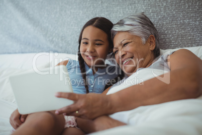 Grandmother and granddaughter using digital tablet in bed room