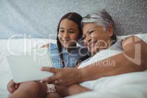 Grandmother and granddaughter using digital tablet in bed room