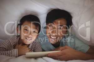 Father and son using digital tablet under blanket in bedroom