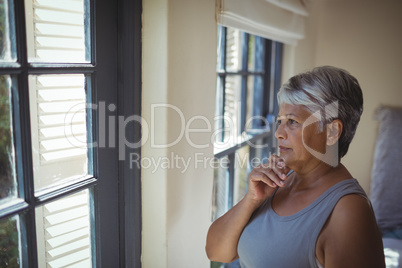 Thoughtful senior woman looking through window in bed room
