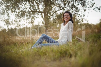 Smiling young woman sitting on grassy field at farm