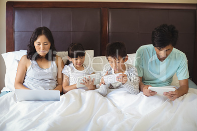 Family using electronic devices in bedroom