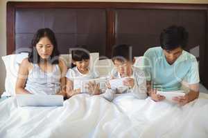 Family using electronic devices in bedroom