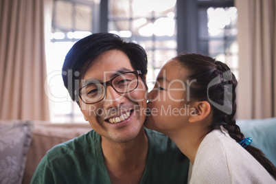 Daughter kissing father on cheeks in living room