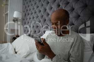 Senior man using mobile phone while sitting on bed