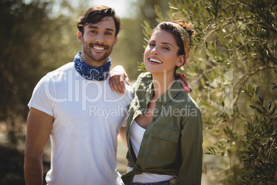 Cheerful young couple standing by trees at farm