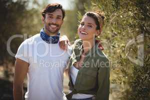 Cheerful young couple standing by trees at farm