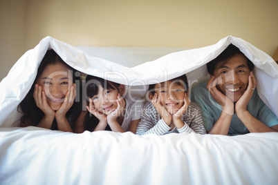 Family relaxing together under a blanket in bedroom